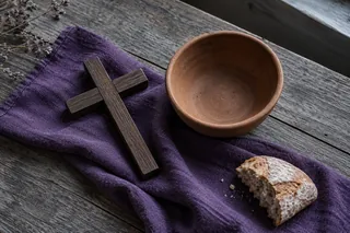 Évocation symbolique du Carême : croix de bois, bol vide et pain sur un linge violet.