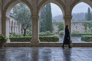 Scène contemporaine imaginée : une femme marche dans un cloître sous une lumière de pluie.