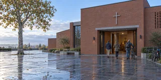 Scène contemporaine imaginée : trois adultes arrivent devant une église de briques après la pluie.