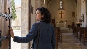Une femme ouvre une porte d’église donnant sur des bancs et un autel.