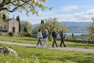 Évocation contemporaine du temps pascal : quatre adultes marchent ensemble près d’une chapelle au printemps.